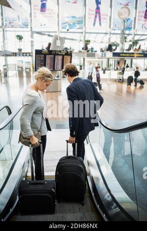 Vista posteriore del personale d'affari con i bagagli che si spostano verso il basso scala mobile in aeroporto Foto Stock