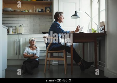 Donna designer industriale che guarda la collega mentre si siede a terra in cucina Foto Stock