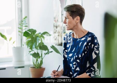 Donna d'affari matura seduta e scrivendo durante la riunione in ufficio Foto Stock
