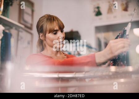 Proprietario che guarda l'abito mentre si sta in piedi al negozio di Thrift Foto Stock