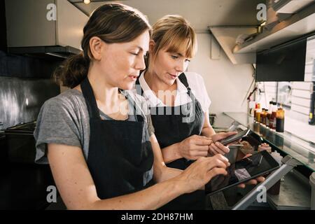 Cuochi femminili che utilizzano la tecnologia nel camion del cibo Foto Stock