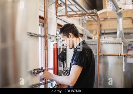 Vista laterale dello studente meccanico automatico che analizza i macchinari in officina Foto Stock