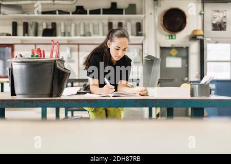 Giovane donna fiduciosa che scrive nel libro all'officina Foto Stock