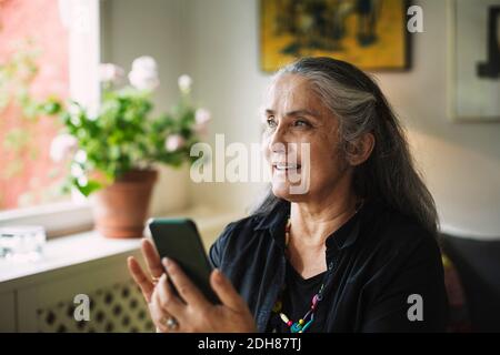 Donna anziana felice che usa il telefono cellulare a casa Foto Stock