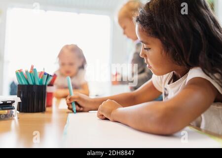 Ragazza con pennarello in classe di disegno con compagni di classe in background Foto Stock