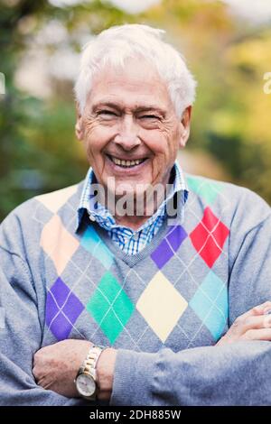 Primo piano ritratto di felice anziano con le braccia incrociate in piedi all'aperto Foto Stock