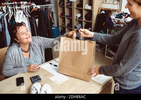 Cassa felice che dà la borsa per la spesa al cliente in negozio di abbigliamento Foto Stock