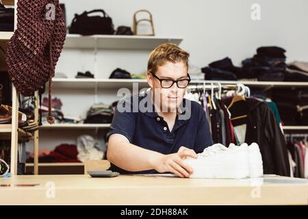 Cassiere che tiene le scarpe sul tavolo durante il calcolo in negozio di abbigliamento Foto Stock