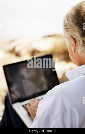 Vista a spalla di un uomo anziano che utilizza un computer portatile all'aperto Foto Stock