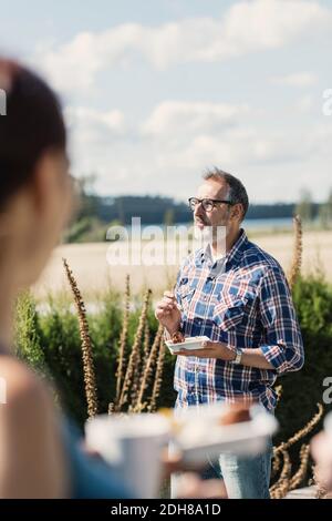 Uomo maturo mangiare cibo con gli amici in cortile sul retro giorno di sole Foto Stock