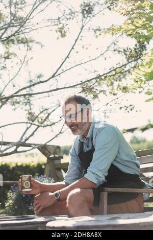 Felice uomo maturo con tazza di caffè seduto in giardino Foto Stock