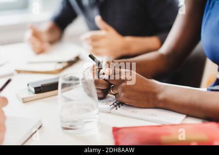 Immagine ritagliata di uomo e donna con smartphone seduto a tavola Foto Stock