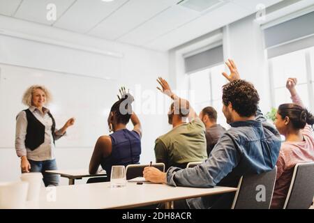 Studenti con braccia alzate guardando l'insegnante in classe di lingua Foto Stock