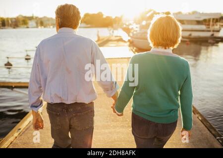 Vista posteriore della coppia senior che tiene le mani mentre si cammina molo Foto Stock