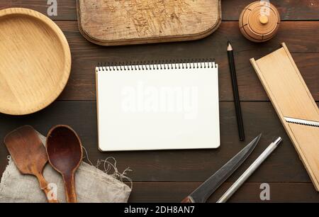 Apri il notebook con le lenzuola bianche vuote e gli utensili da cucina su tavolo di legno marrone Foto Stock