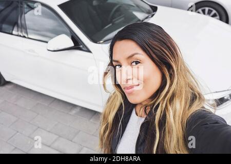 Ritratto ad alto angolo di giovane donna sorridente in piedi contro l'auto Foto Stock