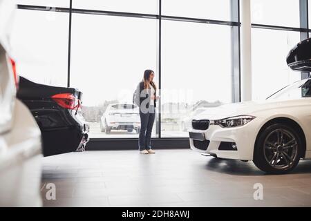 Giovane donna in piedi contro la finestra di vetro presso lo showroom auto Foto Stock