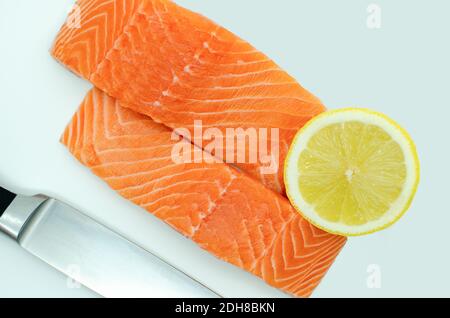 Due fette di filetto di salmone fresco, sfondo bianco vista dall'alto, coltello e limone Foto Stock