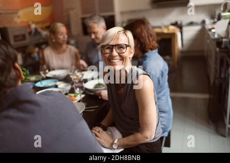 Ritratto di allegra donna matura seduta con gli amici a tavola Foto Stock
