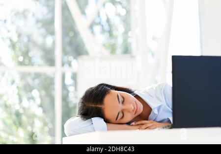 Donna d'affari stanca che dormiva sul posto di lavoro sulla scrivania dell'ufficio Foto Stock