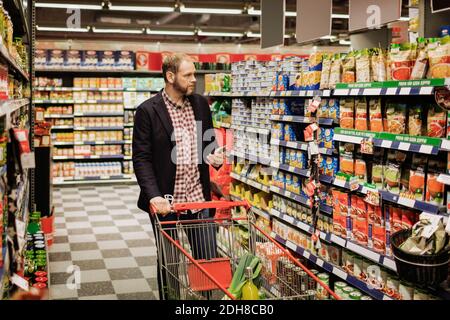 Uomo che usa lo smartphone mentre fa acquisti in un negozio di alimentari Foto Stock