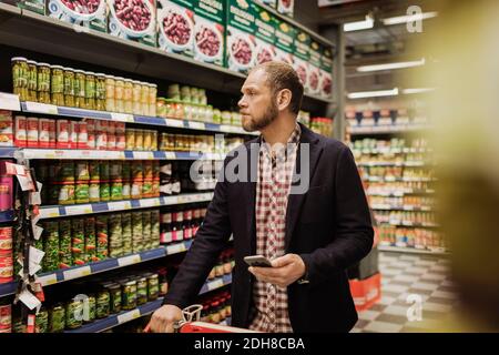 Cliente maschile in possesso di smartphone mentre si acquista in un negozio di alimentari Foto Stock