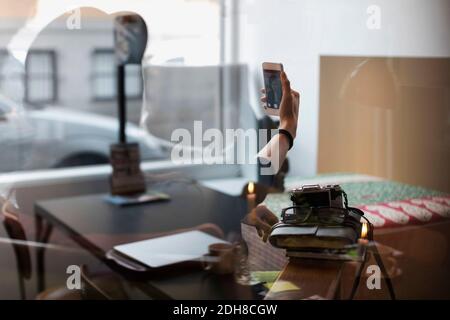 Donna che prende selfie in ufficio creativo visto attraverso il vetro Foto Stock