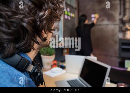 Sezione centrale di uomo d'affari creativo che guarda l'adesivo aderente del collega femminile nota sulla parete Foto Stock