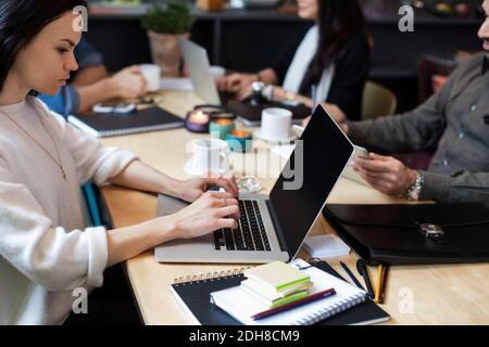 Donna che usa il computer portatile mentre si siede con i colleghi al tavolo Foto Stock