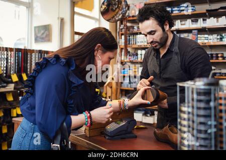 Calzolaio che mostra la scarpa al cliente femminile in negozio Foto Stock