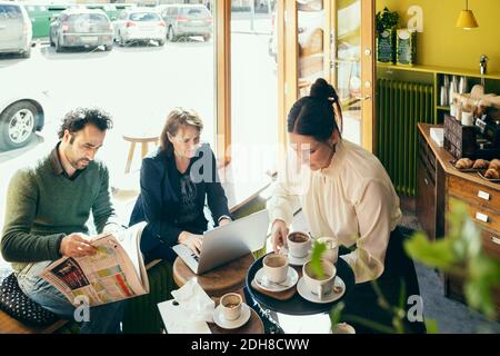 Vista ad alto angolo della cameriera che raccoglie le tazze di caffè mentre clienti seduti al tavolo Foto Stock