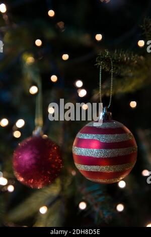 Un primo piano di tradizionali decorazioni di alberi di Natale e baubles appeso su un albero artificiale con luci di fata scintillanti e. spazio di copia Foto Stock