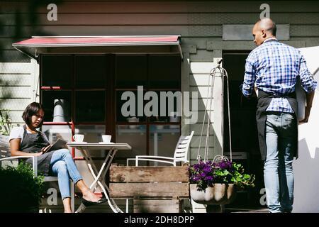 Uomo che cammina verso il bar guardando la collega femminile che lavora tablet digitale Foto Stock
