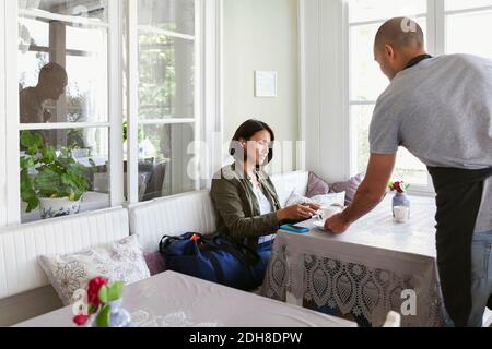 Uomo che serve caffè alla cliente seduto al tavolo caffè Foto Stock