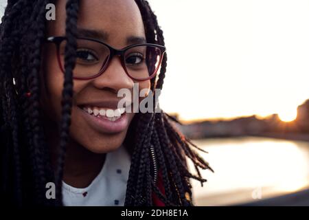 Primo piano ritratto di sorridente adolescente a ponte sul canale contro il cielo limpido in città Foto Stock