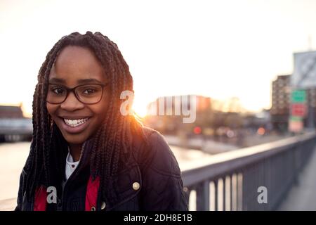 Ritratto di sorridente ragazza adolescente a ponte di canale contro cielo limpido in città Foto Stock
