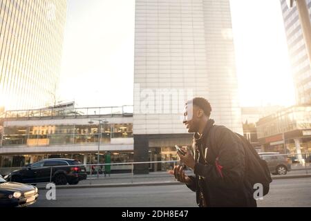 Sorridente adolescente gesturing mentre tiene il telefono contro gli edifici in città Foto Stock