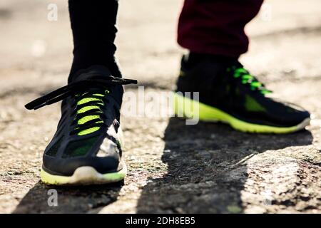 Sezione bassa dell'uomo che indossa scarpe sportive nere in piedi roccia Foto Stock