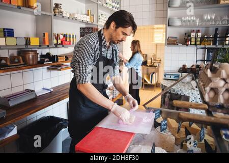 Vista ad angolo alto del proprietario che avvolge il pesce mentre il collega lavora sul mercato Foto Stock