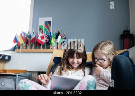 Sorridere agli amici utilizzando il tablet digitale mentre si è seduti sul divano scuola Foto Stock