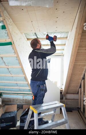 Uomo che fora tavole di legno sulla trave del tetto in casa Foto Stock