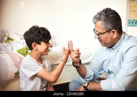 Sorridente padre e figlio che suonano con bande di gomma mentre si siedono a casa Foto Stock