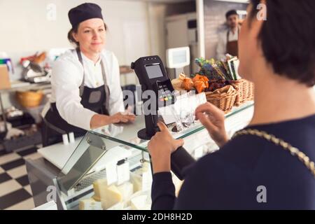 Venditore che guarda il cliente femminile che inserisce il pin nella carta di credito lettore al negozio di alimentari Foto Stock