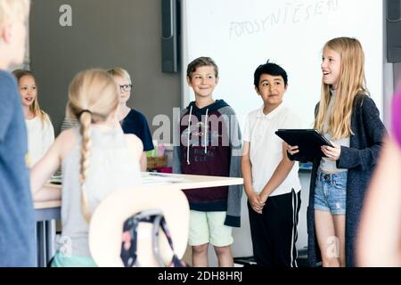 Felice ragazza che dà la presentazione con il tablet digitale tra gli studenti in in aula Foto Stock