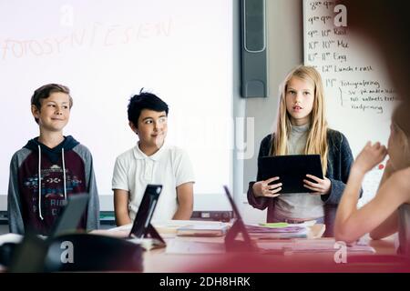 Felice ragazza che dà la presentazione con il tablet digitale tra gli studenti in in aula Foto Stock