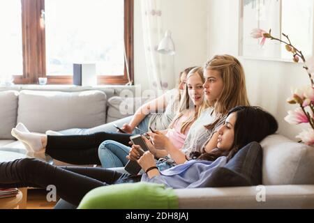 Vista laterale delle ragazze adolescenti che guardano la TV mentre si rilassano divano a casa Foto Stock