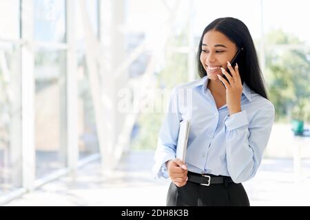 Donna d'affari afro-americana sorridente che parla al telefono in spazio aperto ufficio moderno Foto Stock