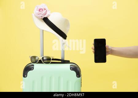 Una vista dall'alto di una valigia, occhiali da sole, telefono e cappello su uno sfondo giallo - concetto di vacanza Foto Stock