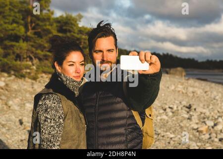 Coppia che prende selfie alla spiaggia durante il tramonto Foto Stock