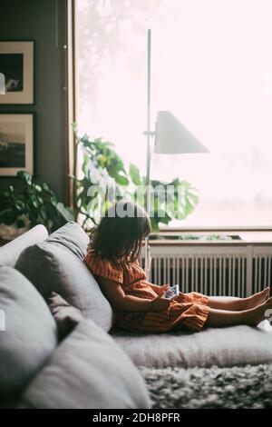 Vista laterale della ragazza sindrome di Down con smartphone mentre seduto sul divano a casa Foto Stock